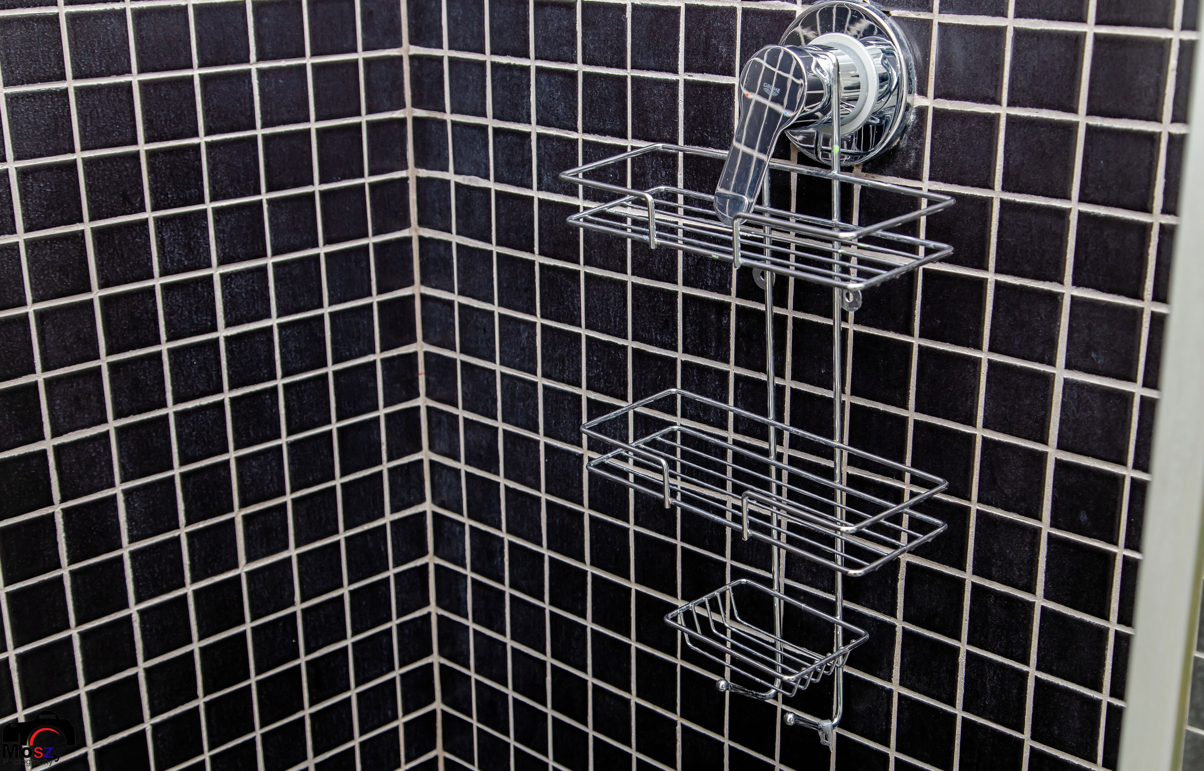 A corner of a room with black tiled walls and a metal shelf unit with a faucet.