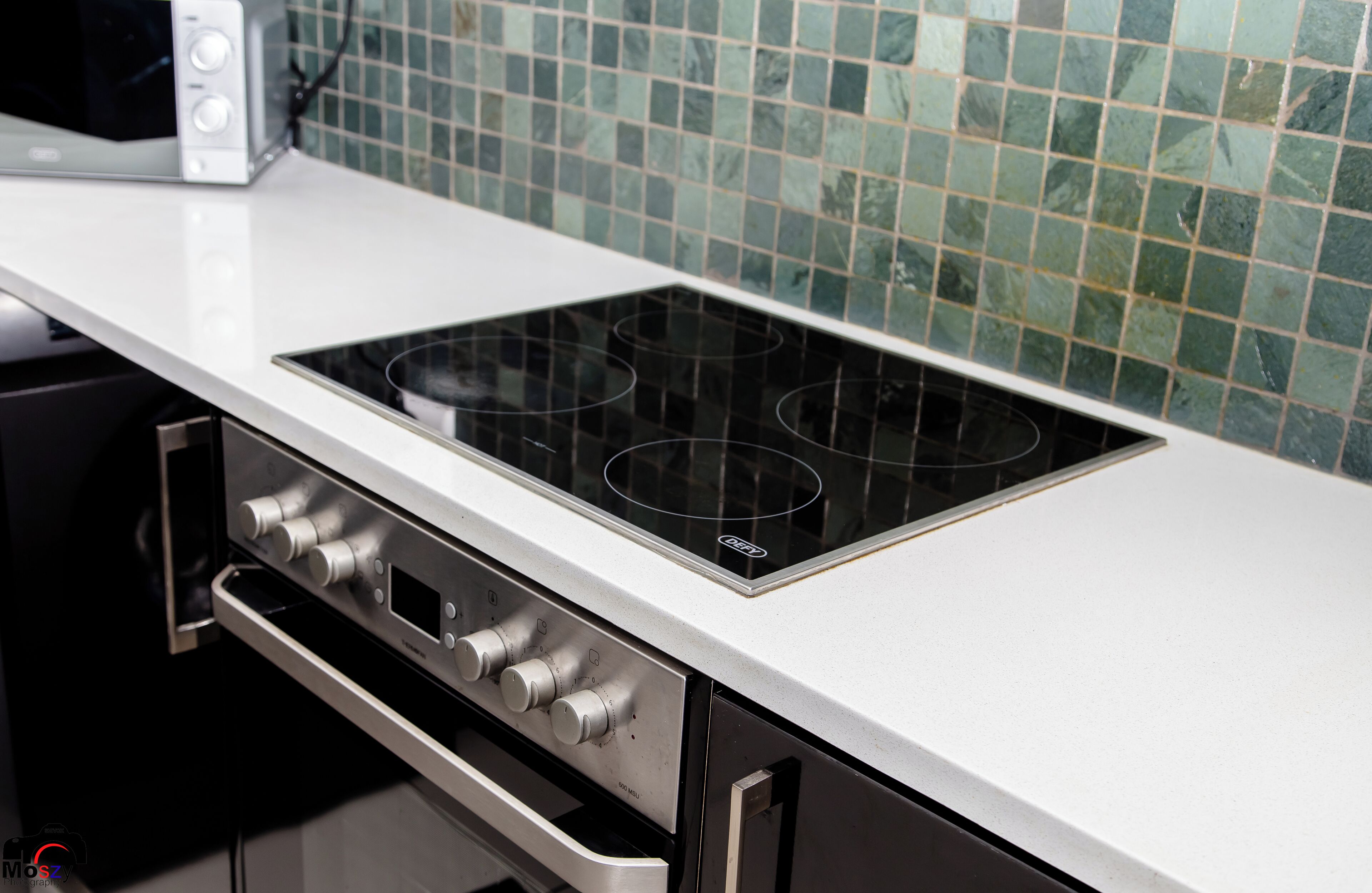 Una cocina con encimera blanca, placa de inducción negra y microondas.