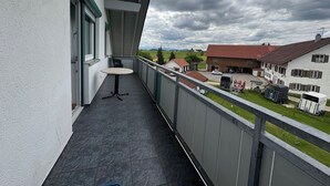 A balcony with a table and chairs, overlooking a parking area and buildings.