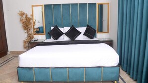 A bed with a teal upholstered headboard, white bedding, and black accent pillows. - Five Seasons Hotel Lahore (Lahore)