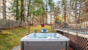 Un bain à remous dans un espace extérieur clos, doté d’une terrasse en bois et d’une piscine en arrière-plan.