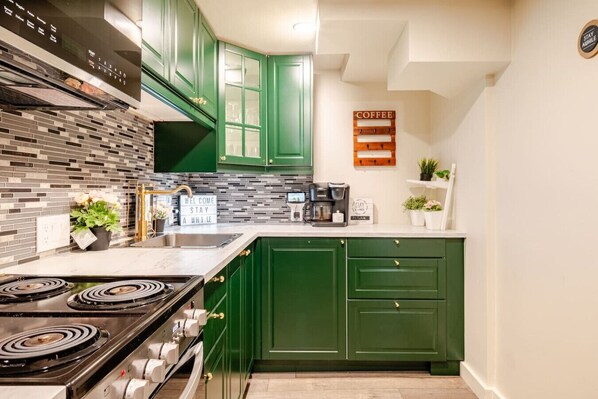A kitchen with green cabinets, a tiled backsplash, a coffee station, and a sign that says "COFFEE".