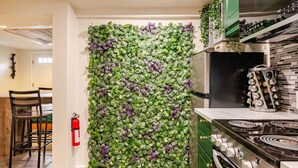 Une cuisine avec un mur décoré de motifs de feuilles vertes et violettes, une cuisinière et un extincteur.