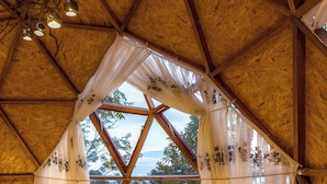 A cozy, naturally lit room with a wooden ceiling, a large window with curtains, a bed, and a wooden chair. - Los Glampings de Taytamaki (Tarapoto)