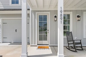 A house with a white garage door, a front door with a glass panel, and a rocking chair outside. - Spacious 6BR Beach Home Sleeps 15 Relax & Reconnect at Coastal Breeze (Panama City Beach)
