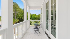 A white porch with a table and chairs, large windows, and a view of greenery. - Spacious 6BR Beach Home Sleeps 15 Relax & Reconnect at Coastal Breeze (Panama City Beach)