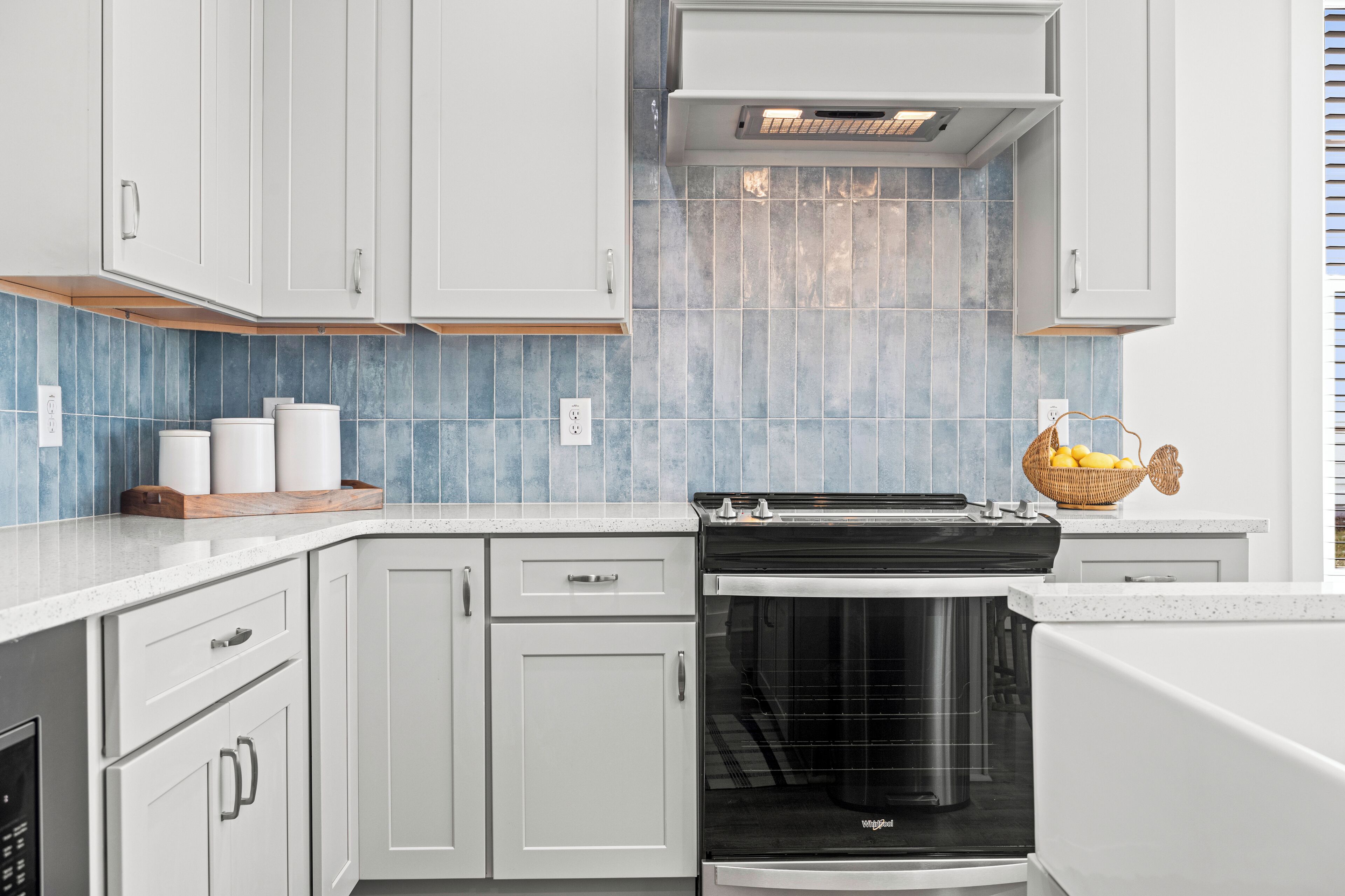 Une cuisine moderne avec des meubles blancs, une cuisinière noire et un dosseret de carrelage bleu.