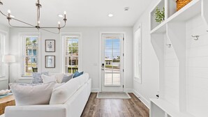 A modern living room with a white sofa, a chandelier, and a view through a door to the outside. - Spacious 6BR Beach Home Sleeps 15 Relax & Reconnect at Coastal Breeze (Panama City Beach)