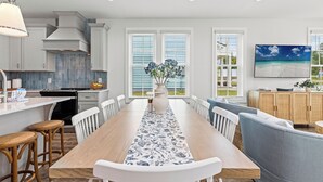 A modern kitchen with white cabinets, a wooden dining table, and a view of the outdoors through large windows. - Spacious 6BR Beach Home Sleeps 15 Relax & Reconnect at Coastal Breeze (Panama City Beach)