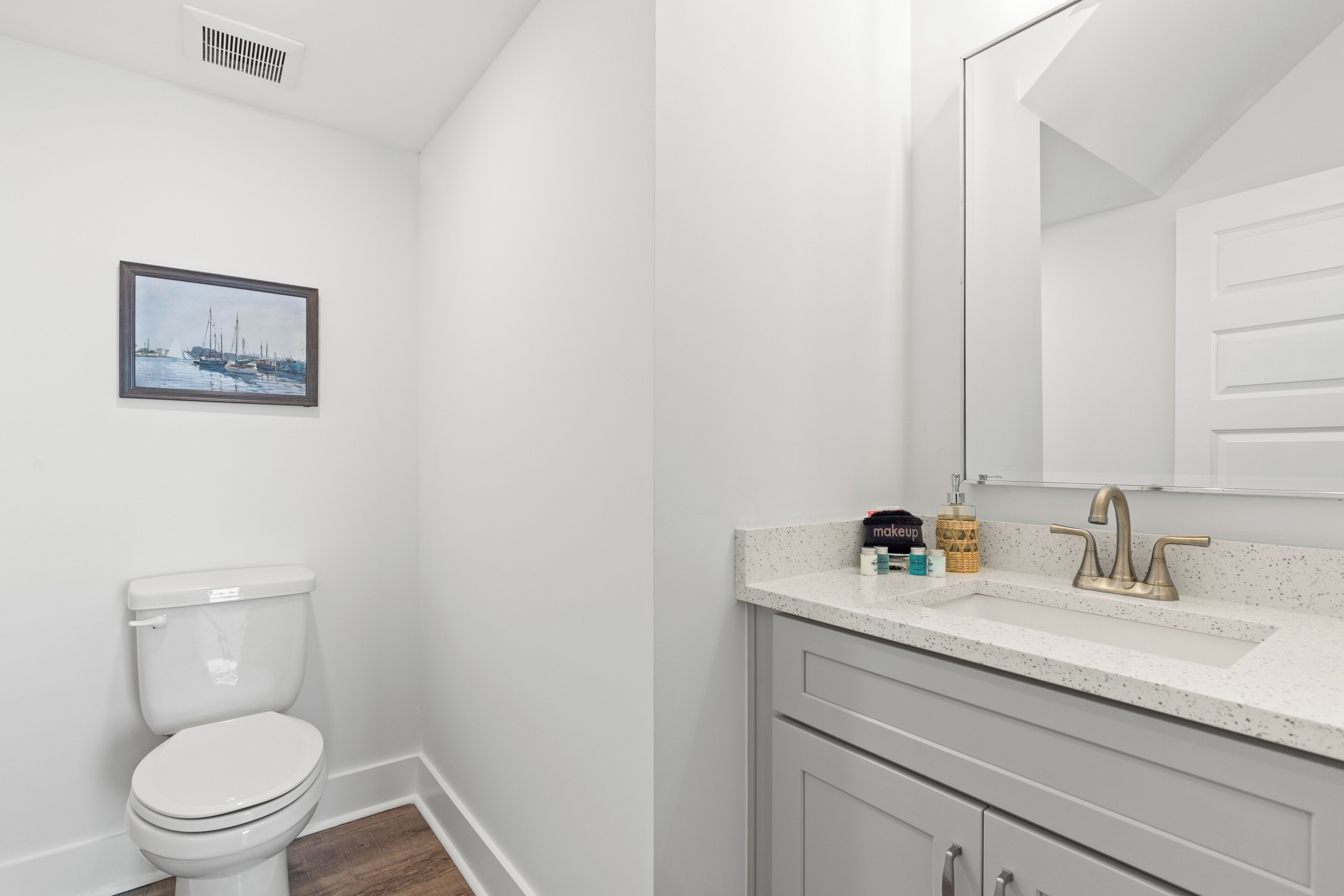A bathroom with a white toilet, a sink with a gold faucet, and a framed picture on the wall.