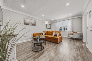 Un salon moderne avec un canapé, une table basse et un fauteuil. Il y a une fenêtre avec des rideaux, une plante et un tableau au mur.