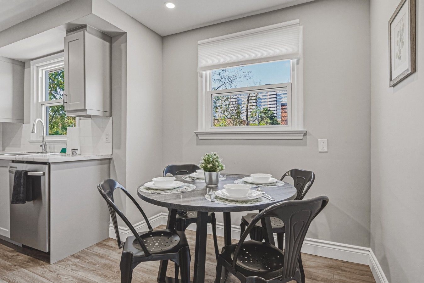 A modern kitchen with a dining area, white cabinetry, and a view through a window.