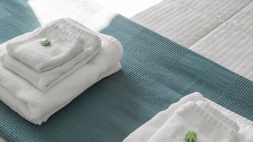 A neatly made bed with a teal bedspread and two folded white towels with green centerpieces.