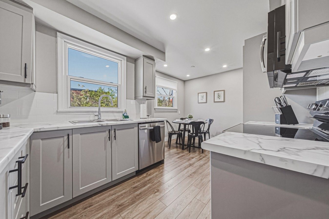 A modern kitchen with a dining area, large windows, and a view of the outdoors.