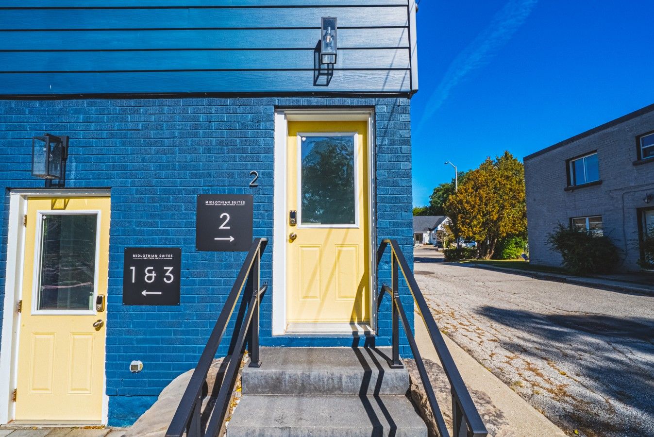 Un bâtiment à la façade bleue, avec des portes numérotées et un escalier bien visible menant à l’entrée.