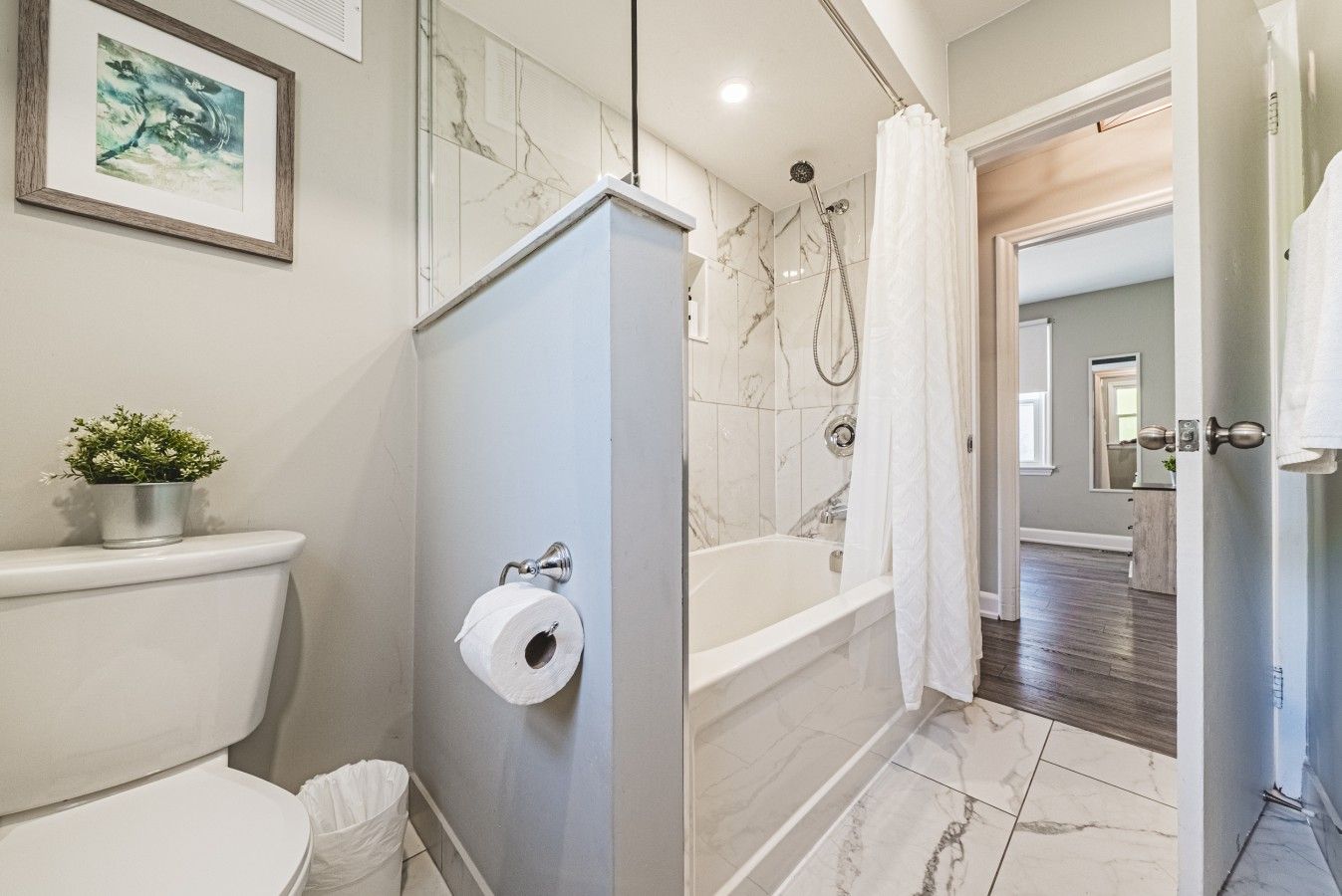 A bathroom with a toilet, a shower with a curtain, a marble-tiled floor, and a framed picture on the wall.