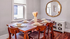 A dining room with a wooden table set for six, a vase with dried flowers, a round mirror, and a white cabinet with shelves. - Hot Tub, Newly Updated, Near DT, Free parking | TS (Peterborough)
