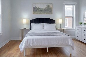 A bedroom with a bed, bedside tables, a dresser, a window, and a painting on the wall. - Hot Tub, Newly Updated, Near DT, Free parking | TS (Peterborough)