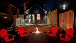 A wooden deck with a fire pit and red chairs, a covered outdoor area, and a building with a sloped roof. - Hot Tub, Newly Updated, Near DT, Free parking | TS (Peterborough)