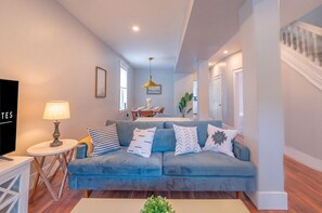 A modern living room with a blue sofa, a small round table with a lamp, and a staircase to the right.