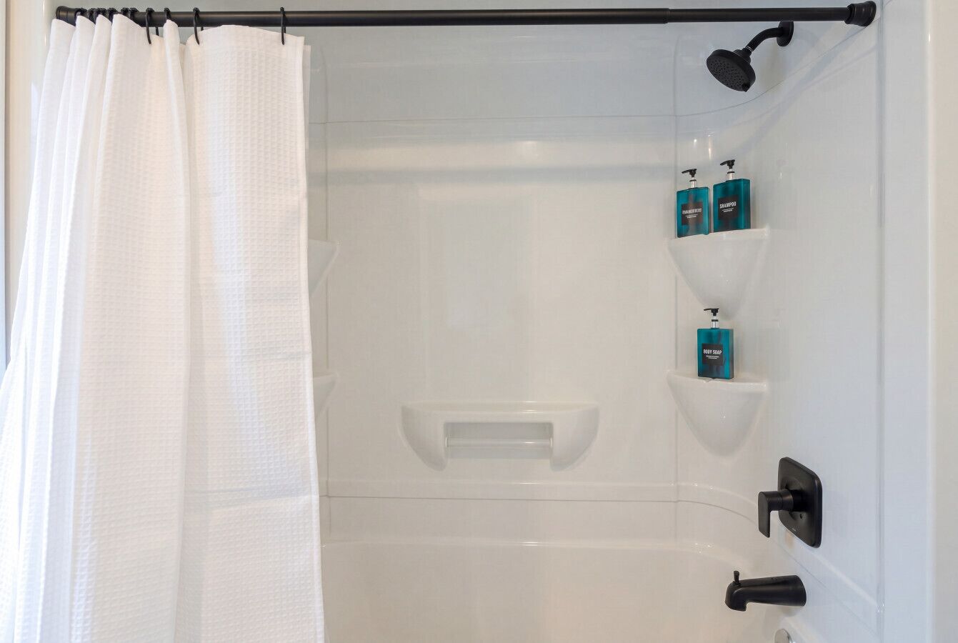 Une douche avec un rideau blanc, un pommeau de douche à main et deux étagères pour les articles de toilette.