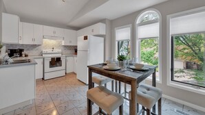 A modern kitchen with white cabinetry, a central island, and a dining area with a wooden table and cushioned benches. - Cozy & Comfortable, Downtown, Parking | TJSI (Burlington)