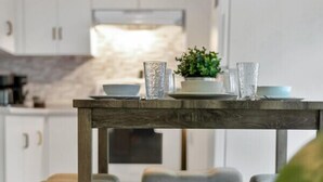 A modern kitchen with white cabinets, a wooden table, and bar stools. - Cozy & Comfortable, Downtown, Parking | TJSI (Burlington)
