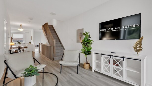 A modern living room with a staircase, a TV displaying 'MIDLOTHIAN SUITES SHORT-TERM RENTALS', and a white console table with decorative items. - Modern Gem, Spacious, Parking | THH (Ajax)