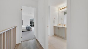 A hallway leading to a bedroom with a bed and a bathroom with a sink and mirror. - Modern Gem, Spacious, Parking | THH (Ajax)