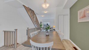 A spacious dining area with a wooden table and white chairs, a staircase with wooden railings, and a green accent wall. - Modern Gem, Spacious, Parking | THH (Ajax)