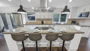 Une cuisine moderne dotée d’un îlot central, de tabourets de bar, de luminaires suspendus et de meubles de rangement blancs.