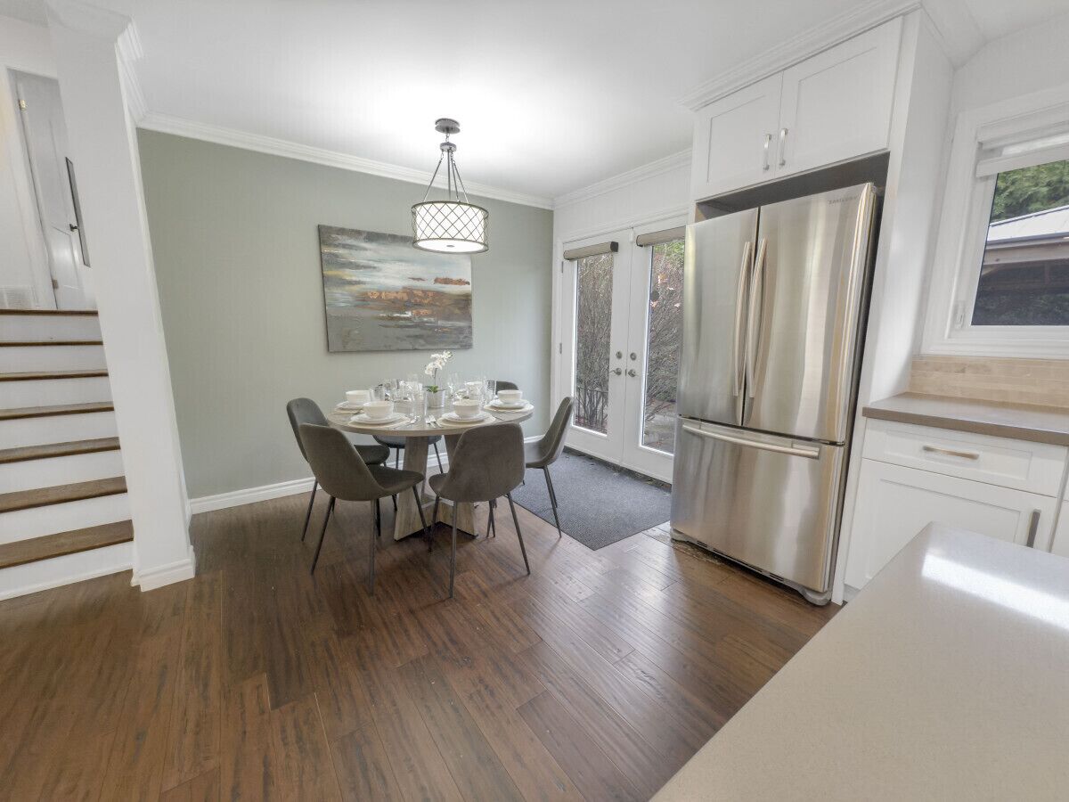 A modern kitchen with a dining area, featuring a stainless steel refrigerator, wooden flooring, and a dining table set for four.