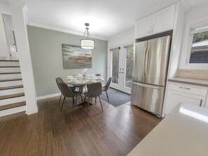 A modern kitchen with a dining area, featuring a stainless steel refrigerator, wooden flooring, and a dining table set for four.