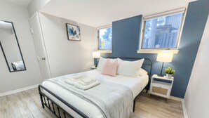 A bedroom with a bed, bedside tables, a window, and a mirror. - Downtown, 2 Bedroom, Parking | TJS3 (Burlington)