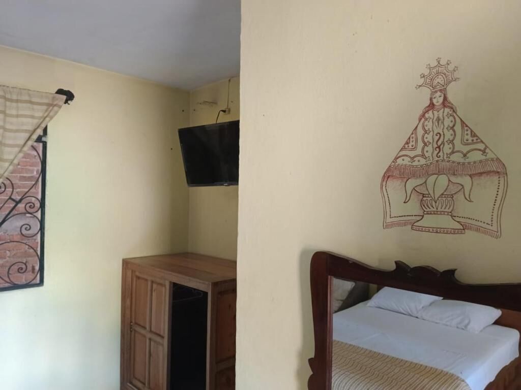 Una habitación con cama, un armario de madera, un televisor montado en la pared y un adorno decorativo en la pared.
