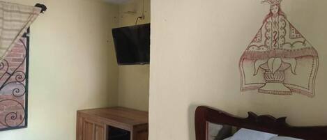 Une pièce comprenant un lit, une armoire en bois, un téléviseur fixé au mur et un élément décoratif mural.