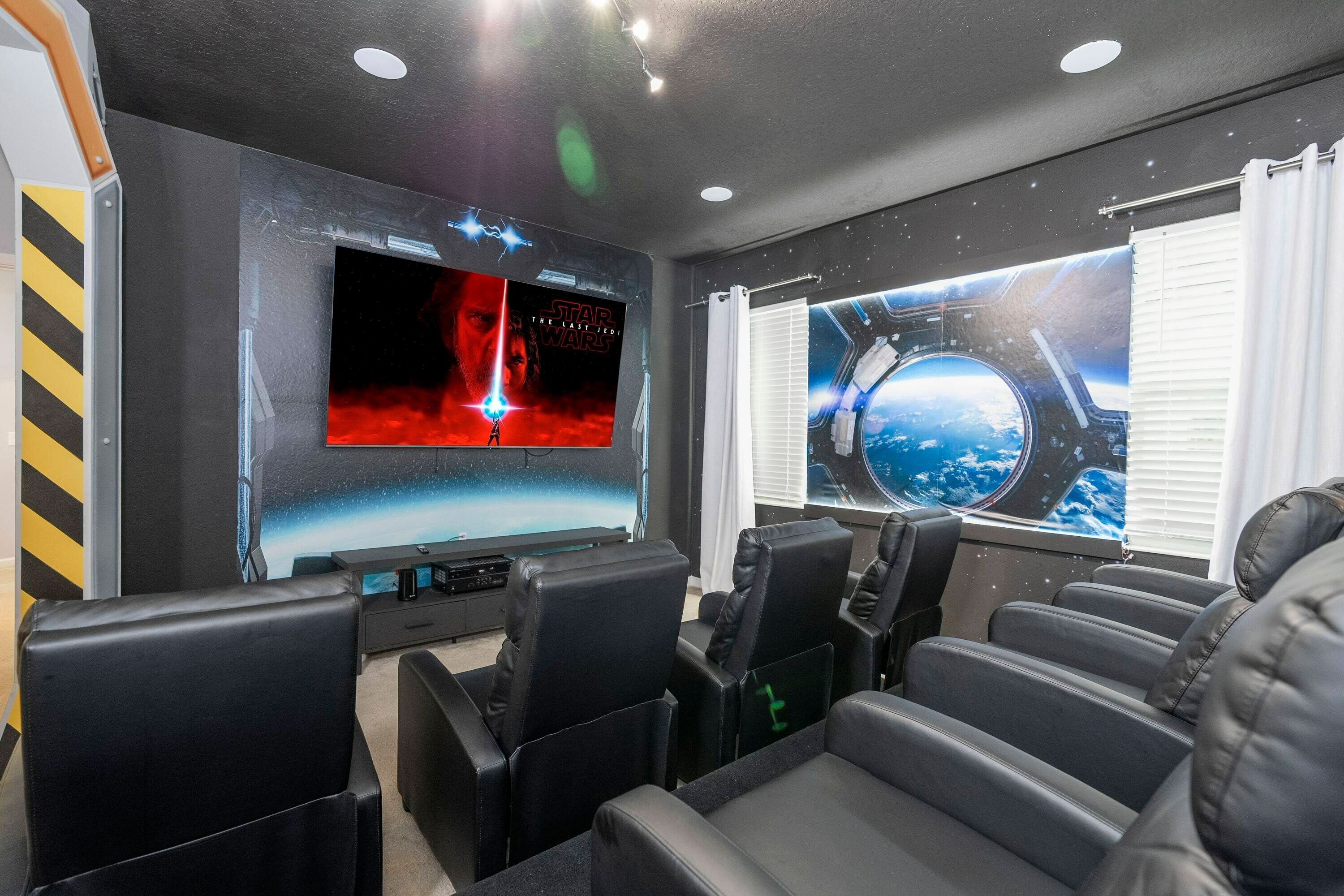 A home theater room with a large flat-screen TV, black leather seating, and Star Wars-themed wall decorations.
