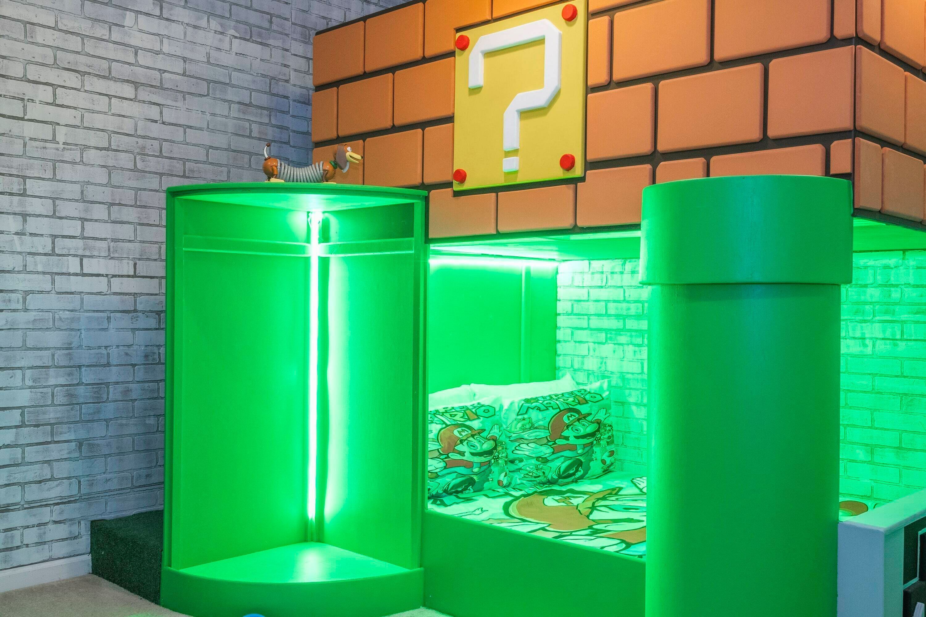 A room with a brick wall, a green-lit play area, and a bed with cartoon-themed bedding.