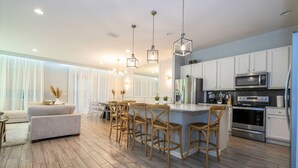 A modern kitchen with white cabinets, stainless steel appliances, and a bar area with wooden stools. - Spacious 12br Family Villa Near Disney Bella Vida (Kissimmee)