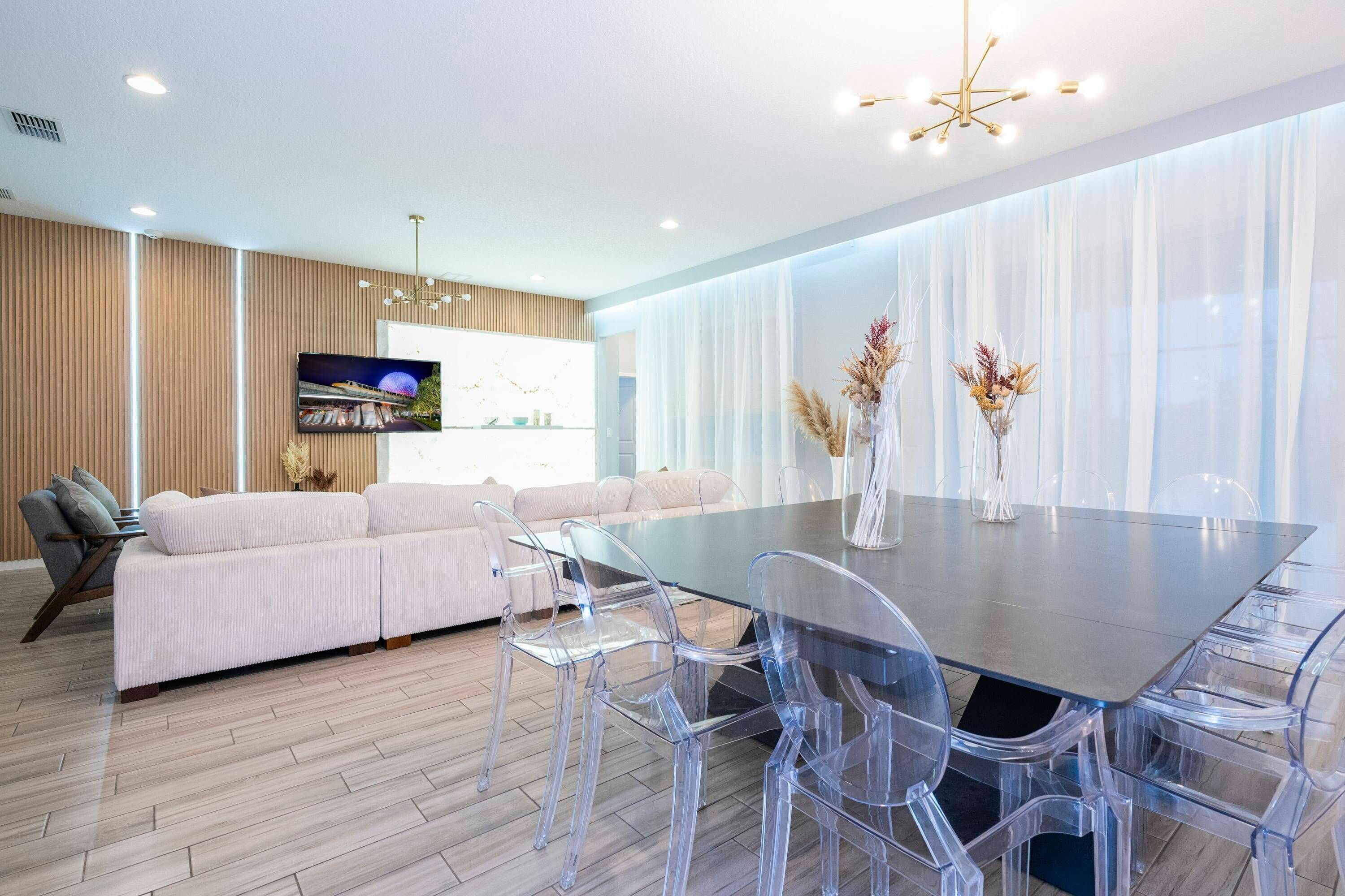 Una sala moderna con un sofá, sillas traslúcidas, una mesa de comedor de vidrio y un televisor en la pared.