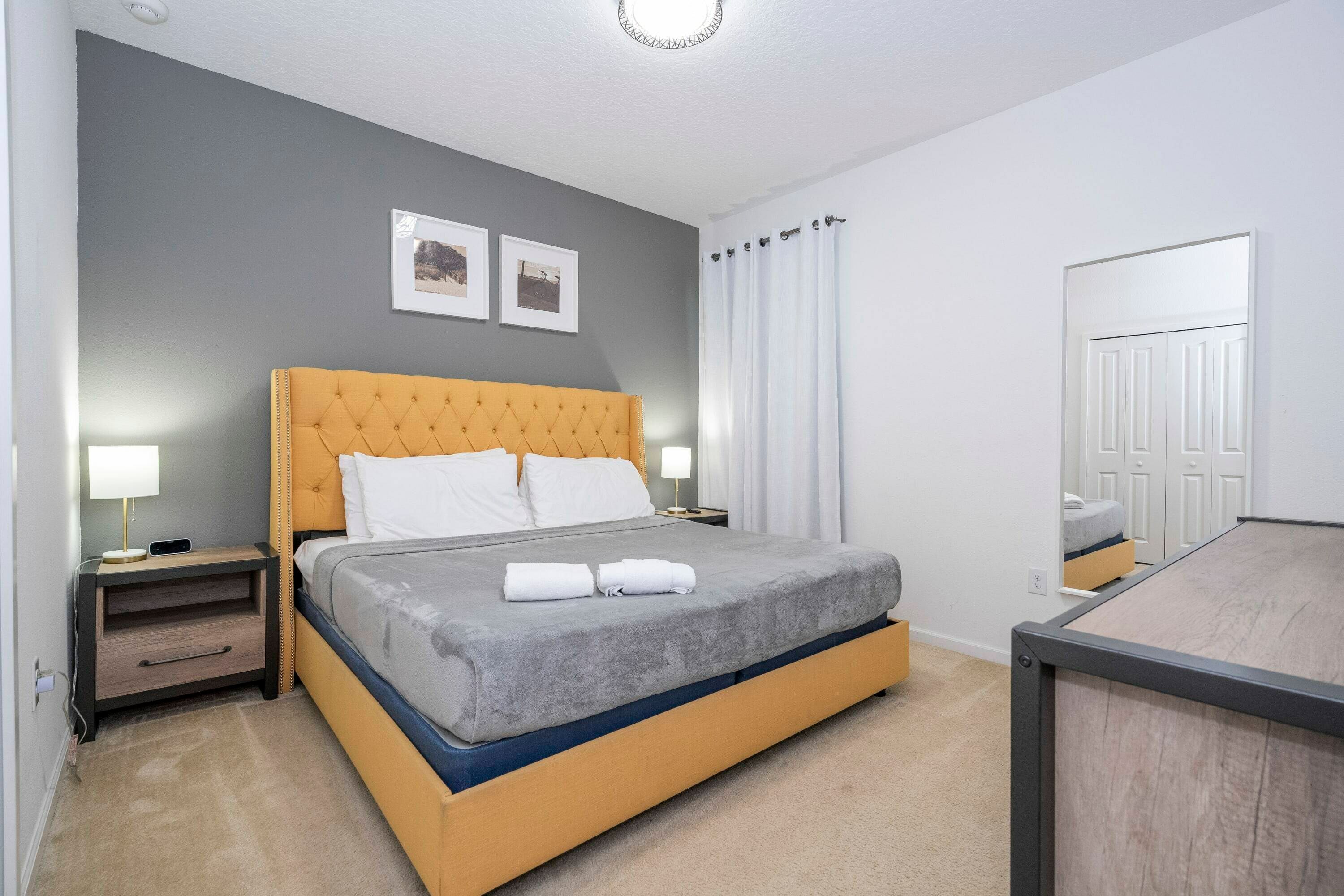 A neatly arranged bedroom with a large bed, bedside tables, and a mirror.