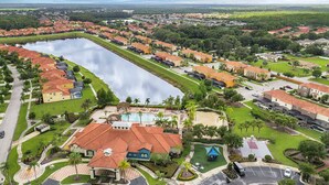 An aerial view of a residential area with a large body of water, houses with red roofs, and a central building with a swimming pool. - Spacious 12br Family Villa Near Disney Bella Vida (Kissimmee)
