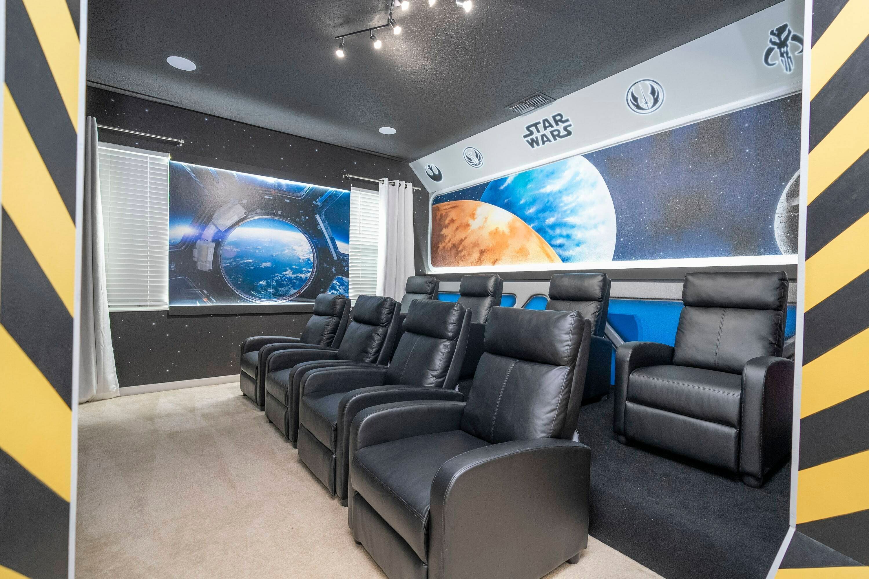 Une salle de cinéma dotée de fauteuils en cuir noir inclinables, d’une grande fresque murale sur le thème de Star Wars et d’une fenêtre avec des stores.