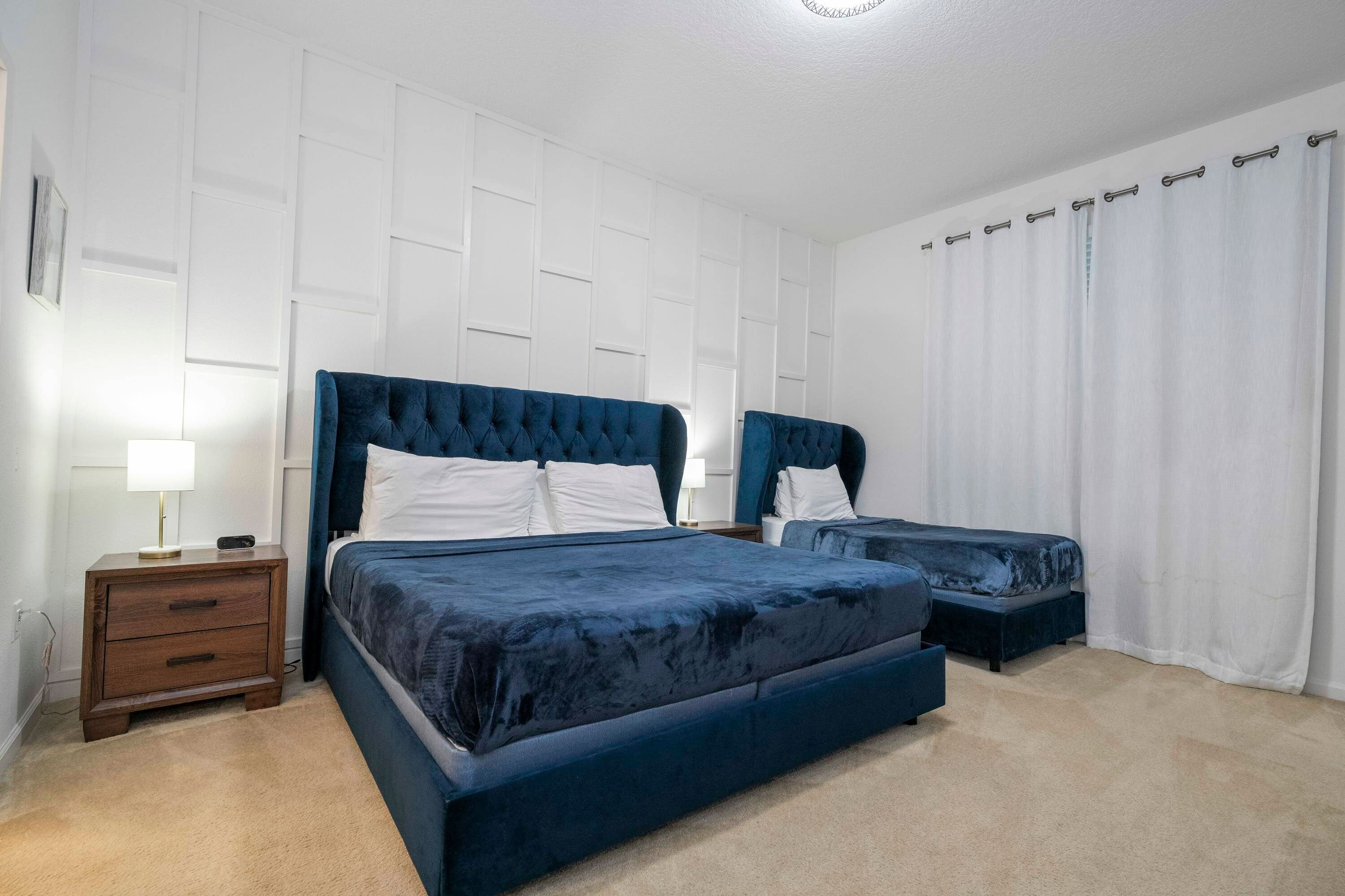 Une chambre avec deux lits, une table de chevet et une grande fenêtre avec des rideaux.