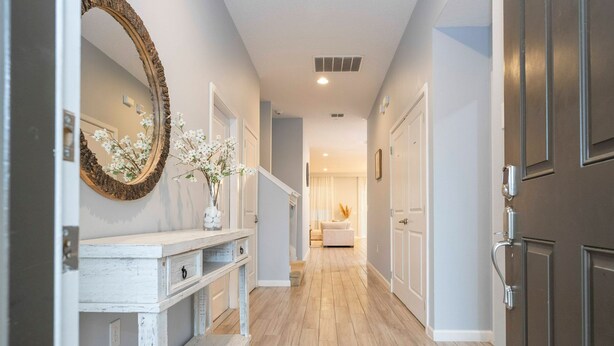 A hallway with a wooden floor, a white console table with drawers, a mirror with a rustic frame, and a door on the right. - Spacious 12br Family Villa Near Disney Bella Vida (Kissimmee)