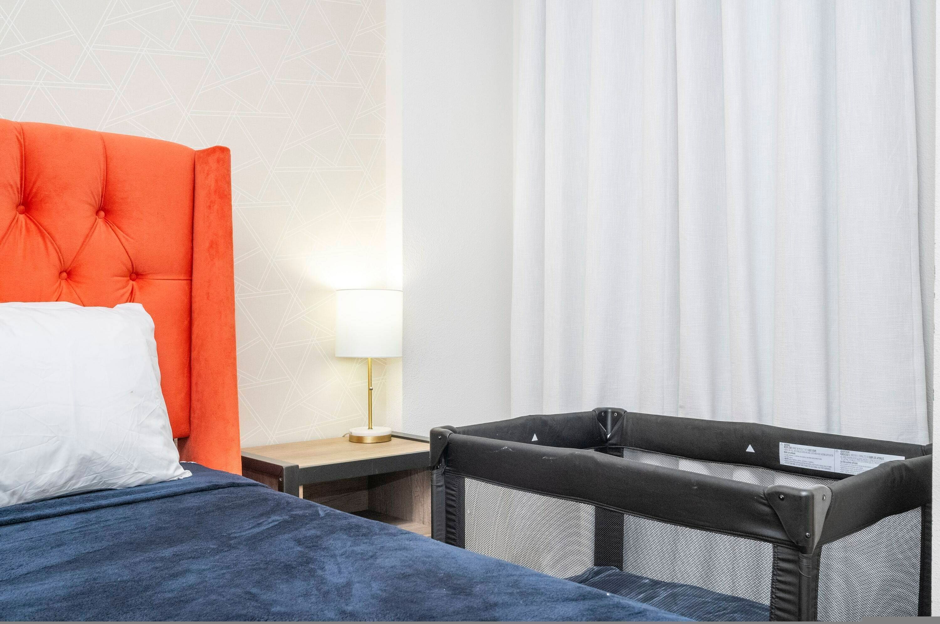 Et hotelværelse med en seng, et natbord, en lampe og en rejsevenkind.