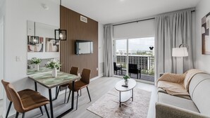 Un soggiorno moderno con zona pranzo, divano, tavolino e vista sulla città attraverso ampie finestre.