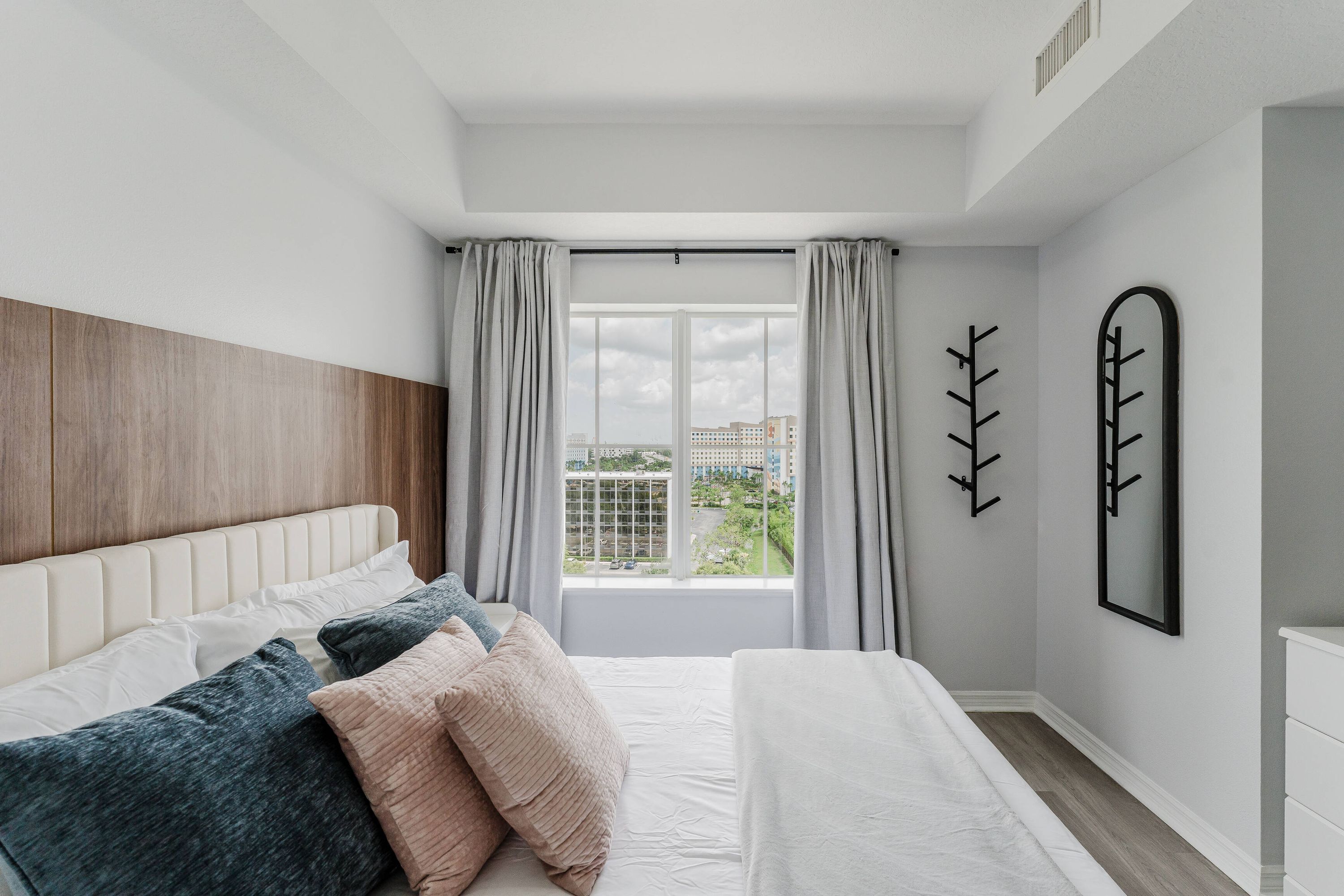 A modern bedroom with a large window, a wooden headboard, and a minimalist decor.