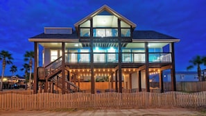 Une maison à deux étages dotée d’un balcon, d’une terrasse en bois et de guirlandes lumineuses.