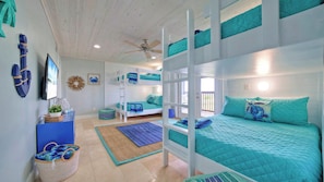 A room with bunk beds, a ceiling fan, a television, and a view of the outdoors. - Sleeps 22 2 Homes w/ Private Pool, Game Room, Nature Views 7 BDR Avantstay (Port Aransas)